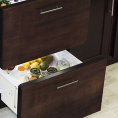 an open drawer in a kitchen filled with fruit and drinks on top of a counter