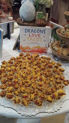 a table topped with lots of tacos covered in cheese and sauce next to a book