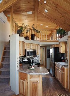 a kitchen and living room in a small house with wood floors, wooden ceilinging and stairs leading up to the second floor