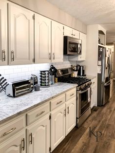 a kitchen with white cabinets and marble counter tops, stainless steel appliances and wood flooring