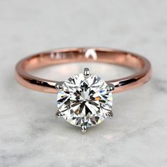 a rose gold engagement ring with a round brilliant cut diamond in the center, on a marble surface