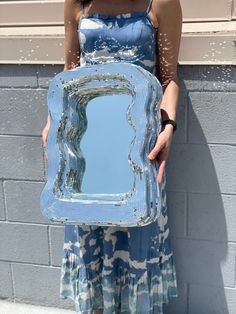 a woman holding up a blue mirror in front of a brick wall with water splashing on it