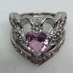 a heart shaped ring with angel wings and pink stones in the center, on a white surface