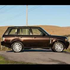 a brown range rover parked on the side of a road in front of a hill