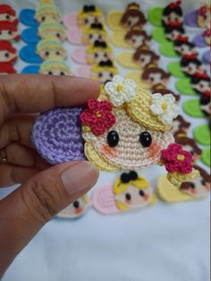 a hand holding a small crocheted doll in front of many other dolls on a table