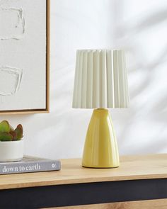 a yellow lamp sitting on top of a wooden table next to a potted plant