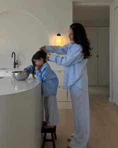 a woman helping a child brush his hair in the kitchen sink while standing on a stool