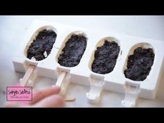 four ice cream popsicles with chocolate frosting in them on a white tray next to a person's hand