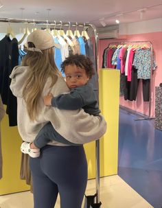 a woman holding a baby in her arms while standing next to a rack of clothes