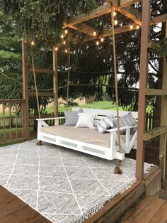 a porch swing with lights hanging from the ceiling and pillows on the ground underneath it