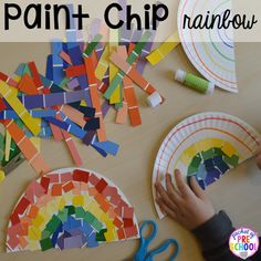 a child's hands holding a paper plate with paint chip rainbows on it