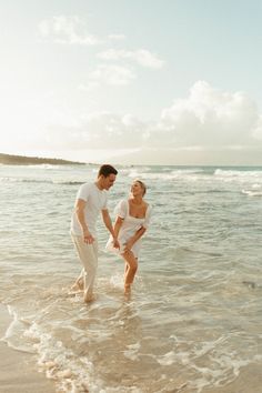 a man and woman standing in the ocean holding hands