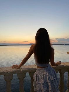 a woman looking out over the water from a balcony at sunset or dawn with her back to the camera