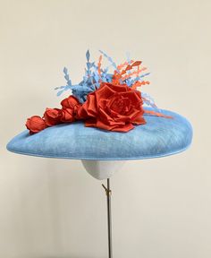 "A stunning pale blue and orange wide brim hatinator.  This gorgeous statement headpiece is made using sinamay straw in a beautiful shade of powder blue. Central to this hat, is a  large handmade silk dupion rose in burnt orange and five matching rose buds that cascade down the brim to one side.  A small collection of powder blue and orange feathers float out  from the top of the rose, adding movement and drama to the overall finished hat.  This particular design has a shallow brim and is secured with a double metal headband that it ribbon wrapped in a colour to blend in with your own hair colour. This band is completely invisible when the hat is on.  Measuring 44cm side to side and 37cm front to back. It is made to a standard 22\" diameter, however, if you require a smaller fit I can prov Blue Feathered Fascinator For Summer, Blue Feather Fascinator For Summer, Blue Feathered Summer Fascinator, Blue Mini Hats With Handmade Flowers For Royal Ascot, Summer Blue Headpiece With Handmade Flowers, Blue Hats With Handmade Flowers For Kentucky Derby, Spring Blue Mini Hats With Handmade Flowers, Blue Fascinator With Curved Brim For Spring, Blue Curved Brim Fascinator For Spring