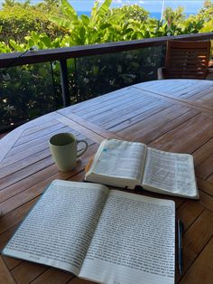 an open book sitting on top of a wooden table next to a cup and pen