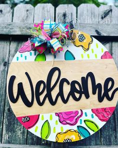 a welcome sign on the side of a wooden fence with flowers and leaves painted on it