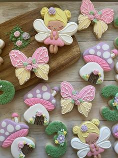 decorated cookies are arranged on a cutting board with fairy figurines in the background