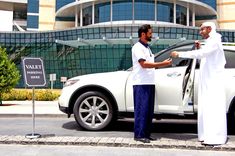 two men shaking hands in front of a white car