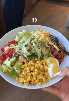 a person holding a white bowl filled with salad and an egg on top of it