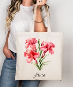 a woman holding a tote bag with pink flowers on it and the name jesus