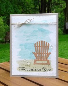 a card with a wooden chair on the beach in front of some grass and trees