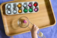 a child playing with an egg carton filled with pom - poms on a table