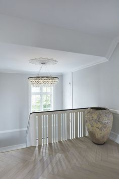 a large vase sitting on top of a hard wood floor next to a window in a white room