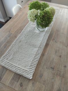 a wooden table topped with a glass vase filled with flowers next to a white crocheted runner