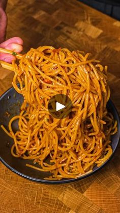 someone is holding chopsticks over a plate of noodles on a wooden counter top