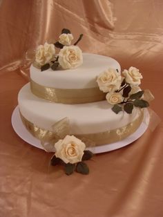 three tiered wedding cake with white roses on top and gold ribbon around the edges