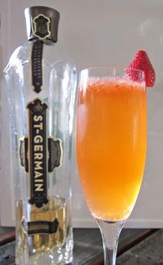 a glass filled with orange juice next to a bottle and strawberries on the table