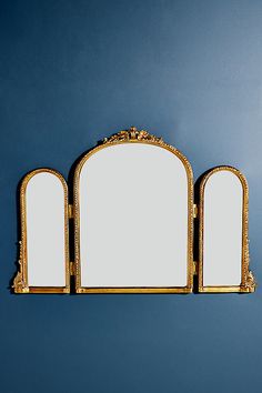 three mirrors are placed next to each other on a blue wall with gold trimmings