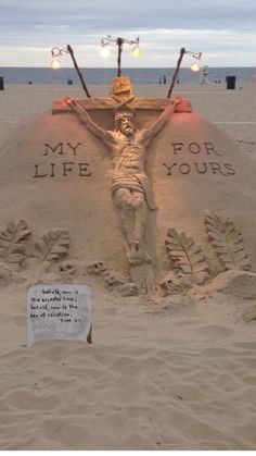 a sand sculpture depicting jesus on the cross with words written in it and lights above him