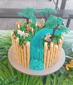 a cake decorated with animals and trees on top of a table next to a bench