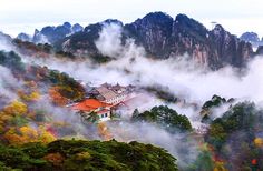 the mountains are covered in fog and low lying clouds, with houses nestled among them