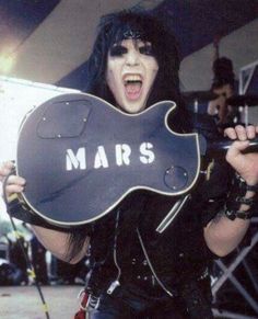 a man with black hair holding a guitar in front of his face and wearing leather clothes