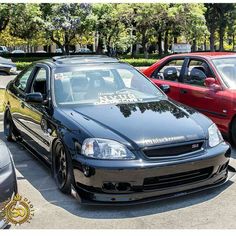 two cars parked next to each other in a parking lot with trees and bushes behind them