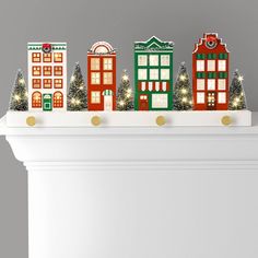 a white mantle topped with christmas decorations and lit up town houses on top of it