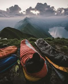 two sleeping bags sitting on top of a mountain next to a body of water with mountains in the background