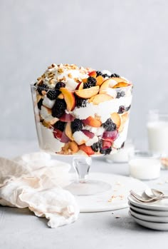 a dessert with fruit and whipped cream in a glass dish on a table next to plates