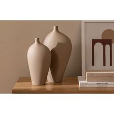 two white vases sitting next to each other on a wooden shelf near a framed photograph