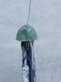 a green jellyfish hanging from a hook on a white wall with multicolored yarn