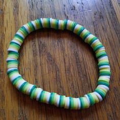 a green and white striped bracelet sitting on top of a wooden table next to a cell phone