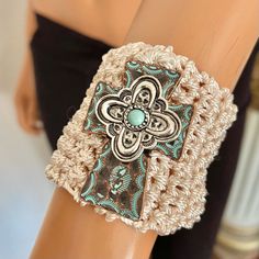 a crocheted bracelet with an ornate cross on the front, and a turquoise bead in the middle