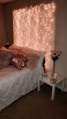 a white bed topped with lots of pillows next to a window covered in fairy lights