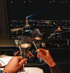 two people toasting with wine glasses in front of the eiffel tower at night