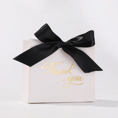 a white box with a black ribbon and thank you written on the front in gold foil