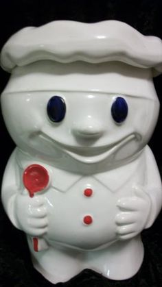 a white ceramic toy with blue eyes and a hat on it's head holding a red object