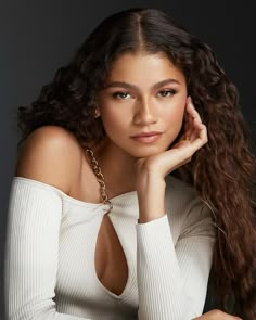 a beautiful young woman with long hair wearing a white top and holding her hand on her shoulder