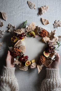 an arrangement of fruit and leaves arranged in the shape of a wreath on a table